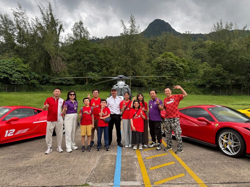 獅友、家長與小戰士在直升機前合照，兩旁停泊紅色跑車，背景為山巒